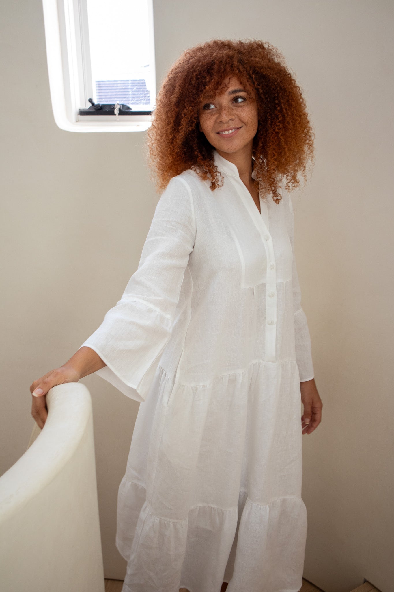 model wearing beautiful white linen dress at the top of her stair case 