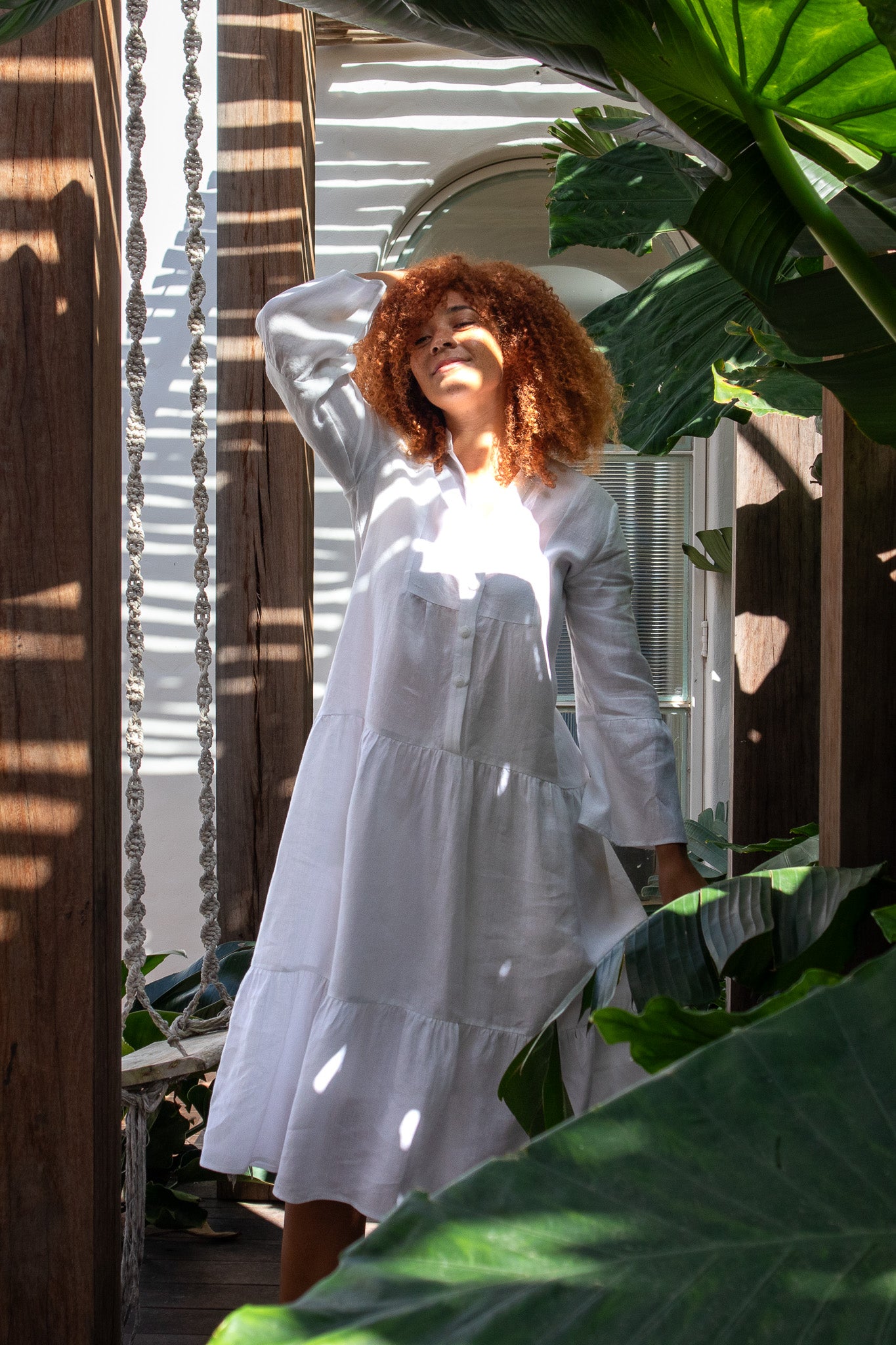 Model wearing a white linen dress with the sun coming through her garden hitting her face 