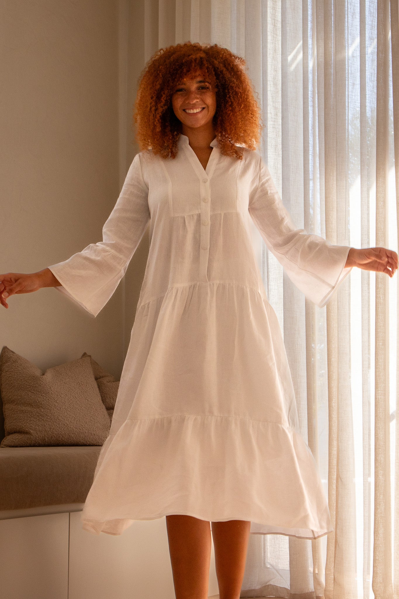 Model in a white linen dress holding her hands out to her side showing bell sleeves on the dress 