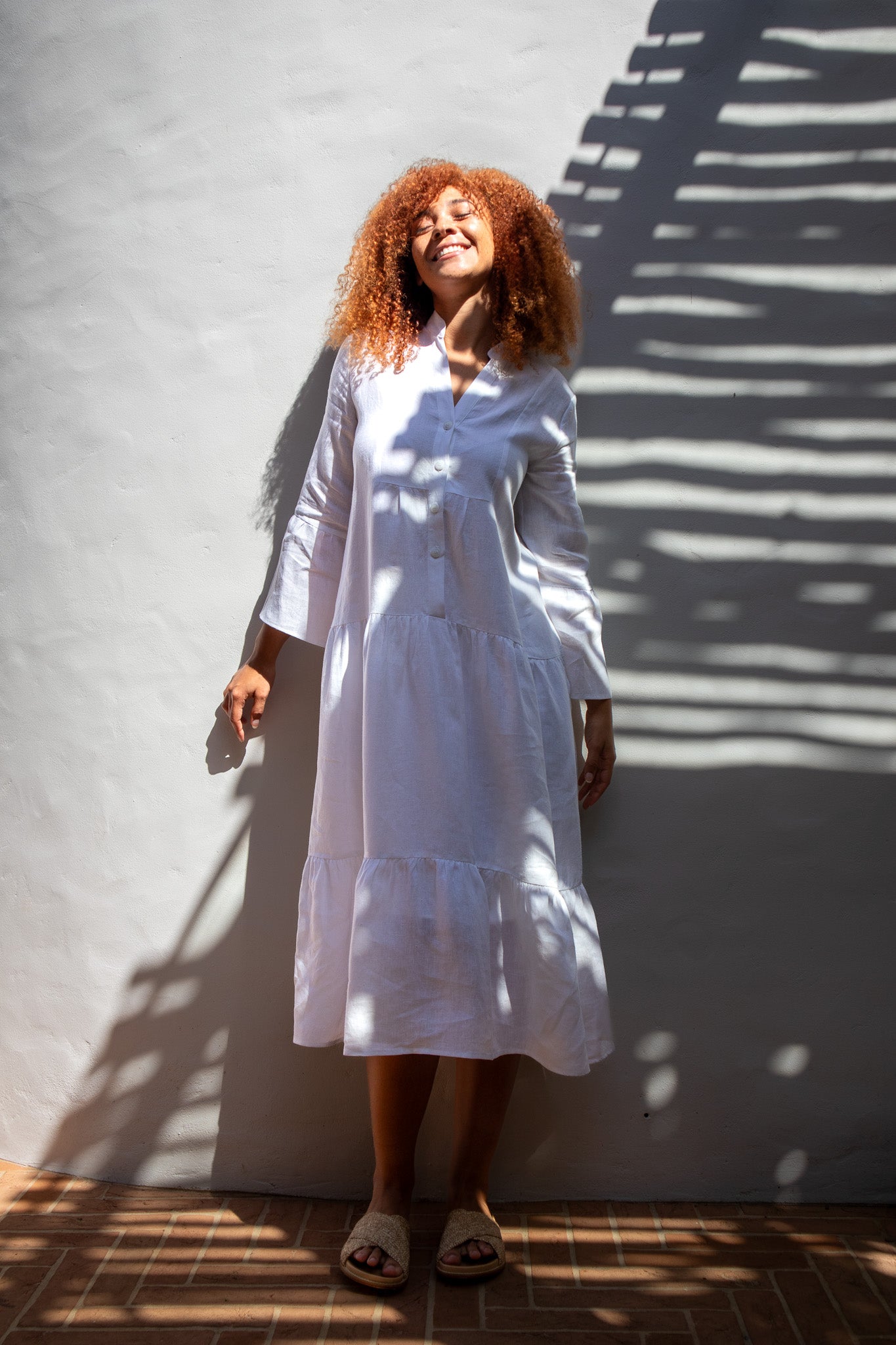 Model looking happy in a beautiful white linen dress with the sun on her face