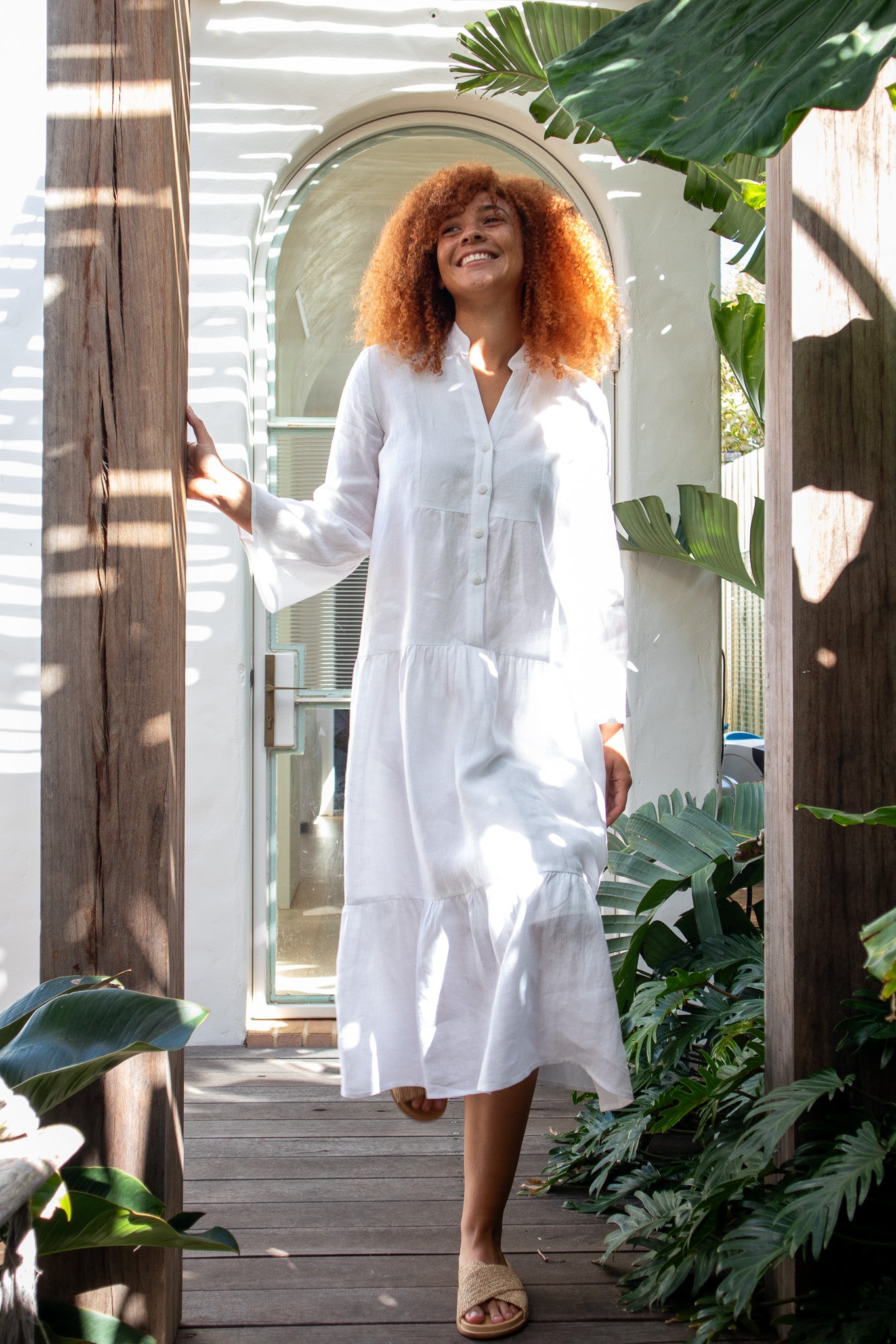 Lady walking in a white linen dress with a big smile looking happy 