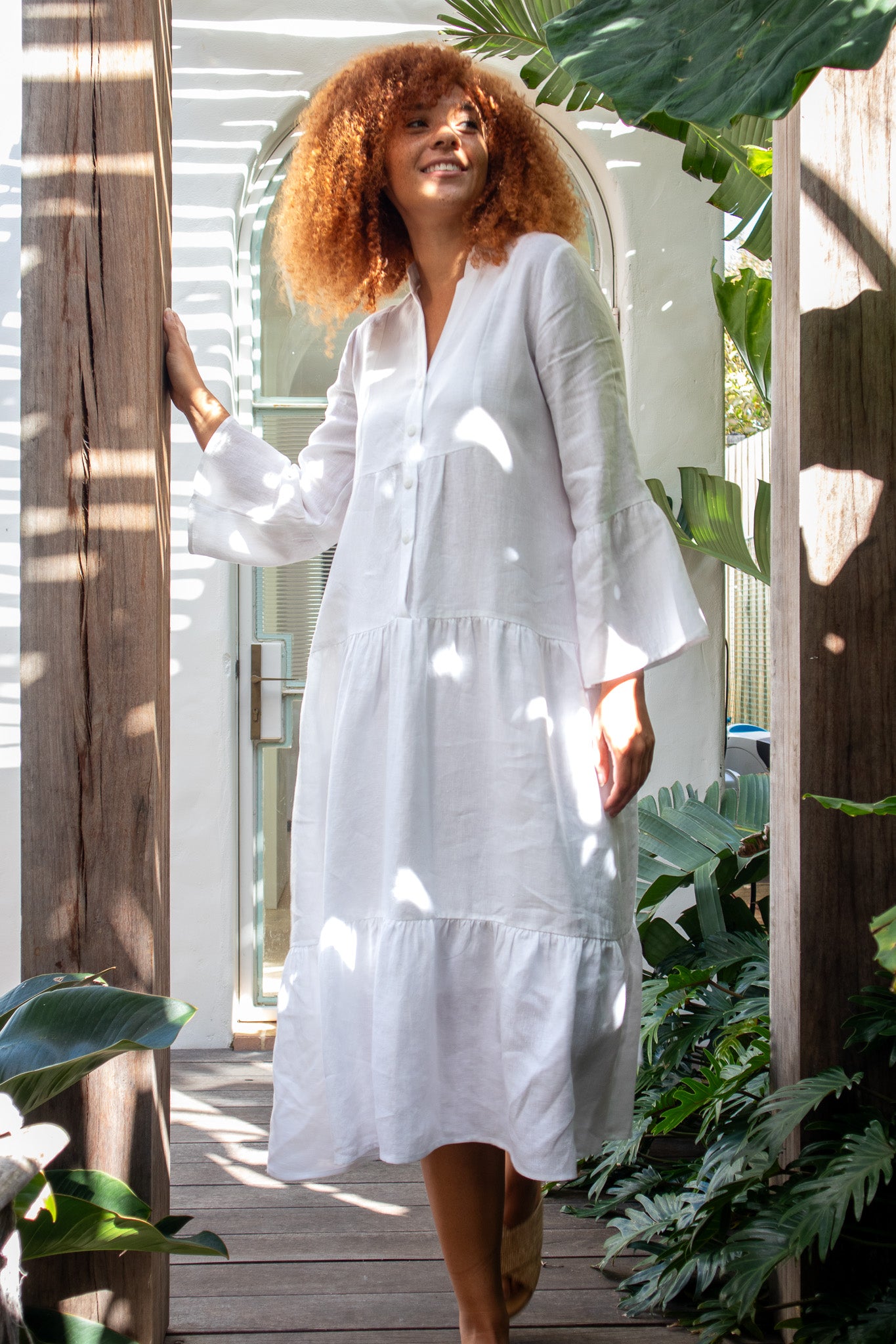 lady walking in a white linen dress under a terrace looking of to the distance 