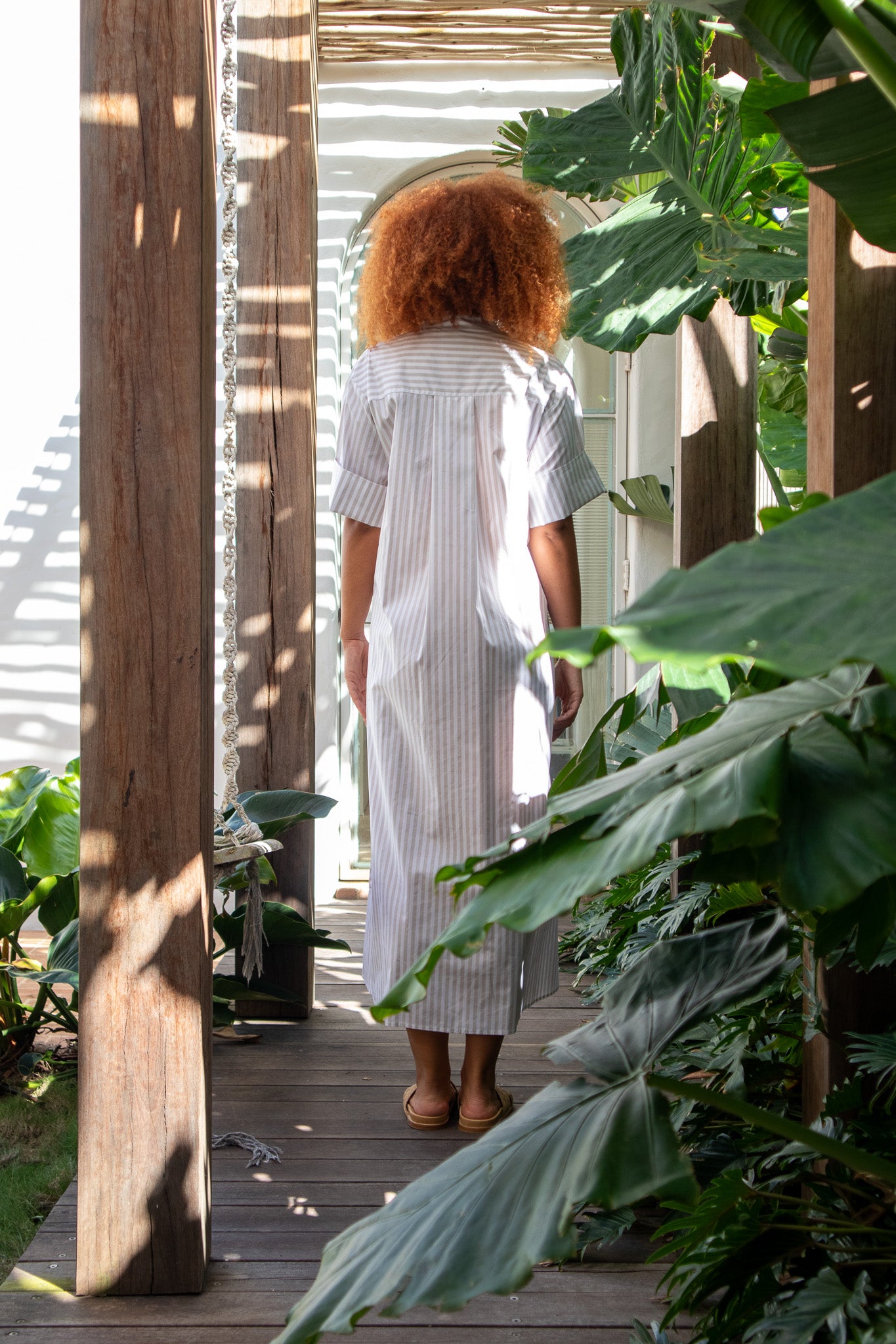 Model showing the back details of a beige stripe dress with arms by her side