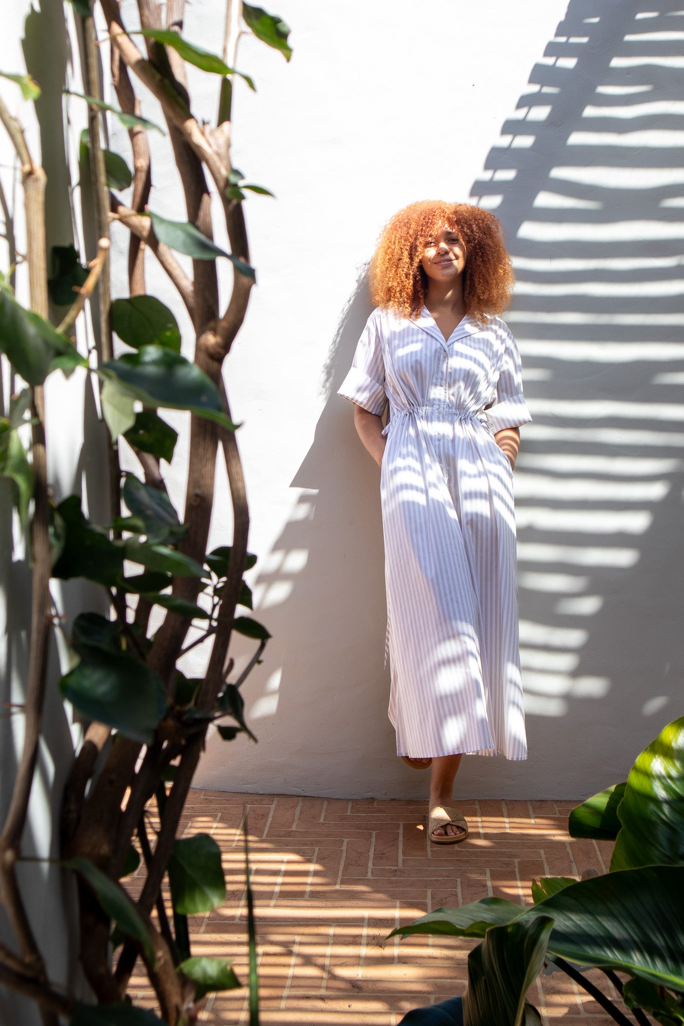 Model leaning up against the wall, hand in pockets, wearing beige stripe dress 