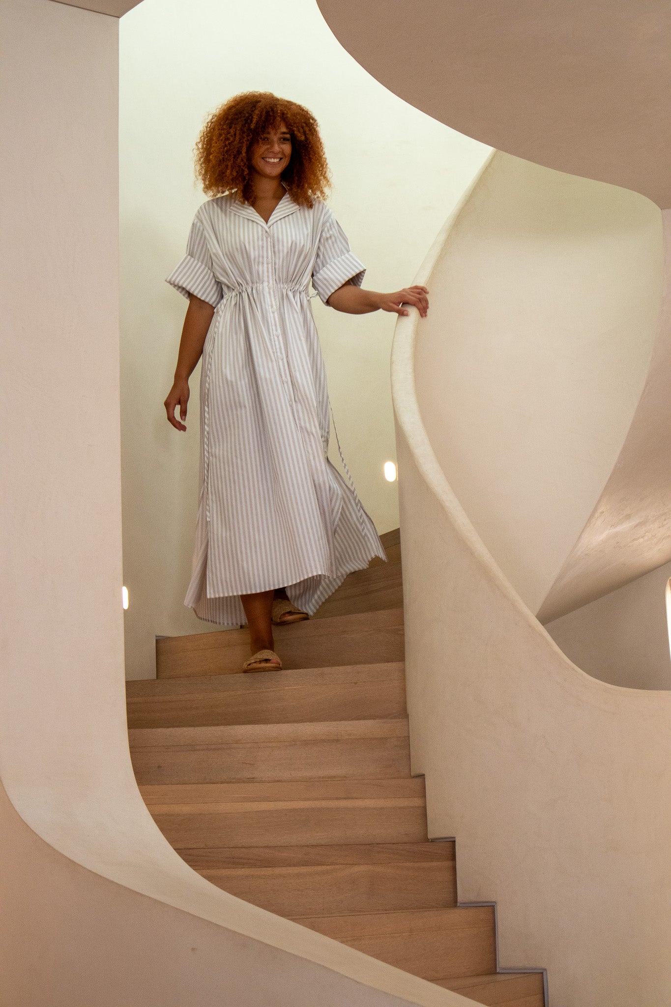 Model smiling walking down the stairs wearing beige stripe dress 